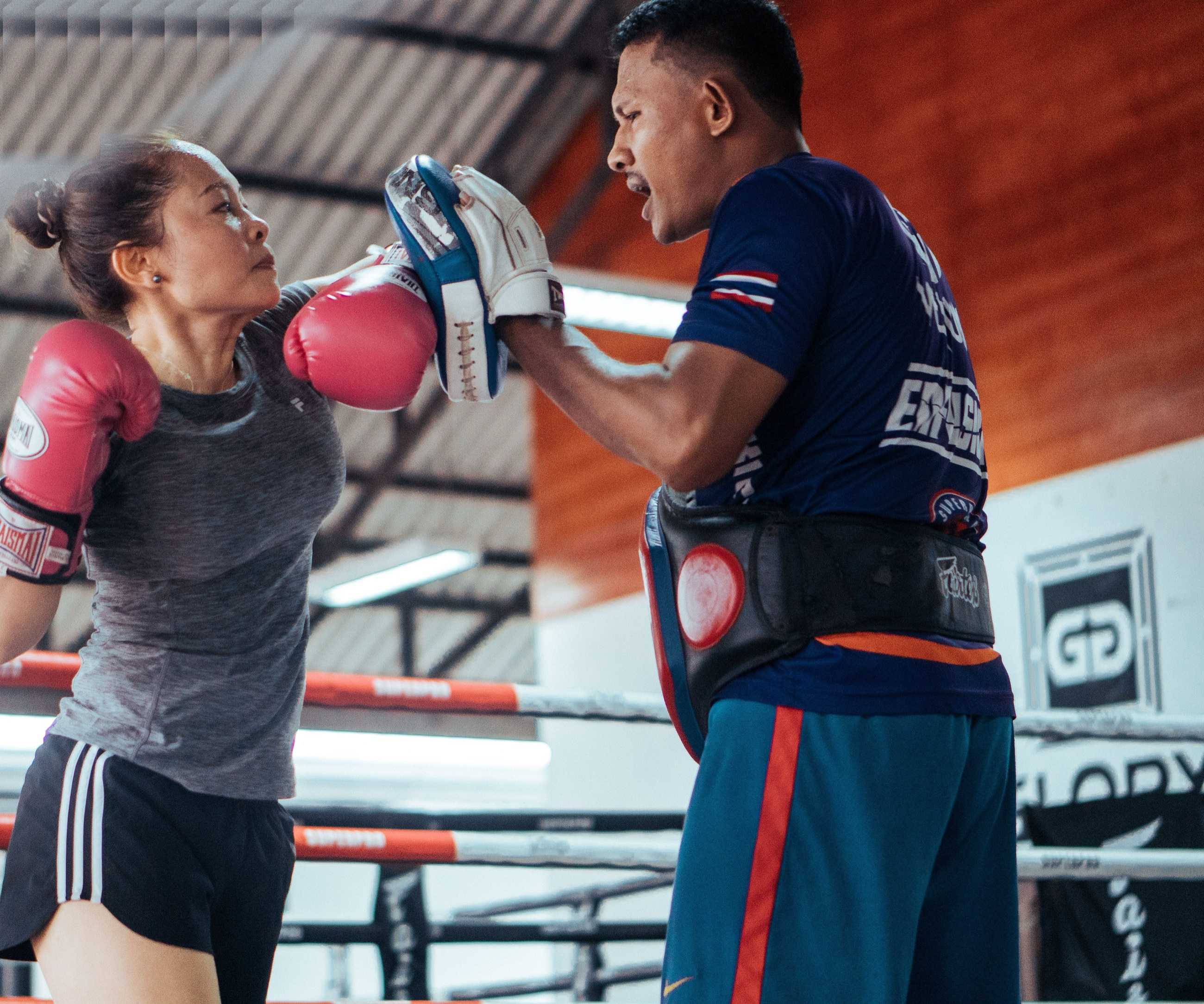 A Thai coach holding focus mitts for a woman throwing a punch in a Muay Thai gym in Chiang Mai, Thailand
