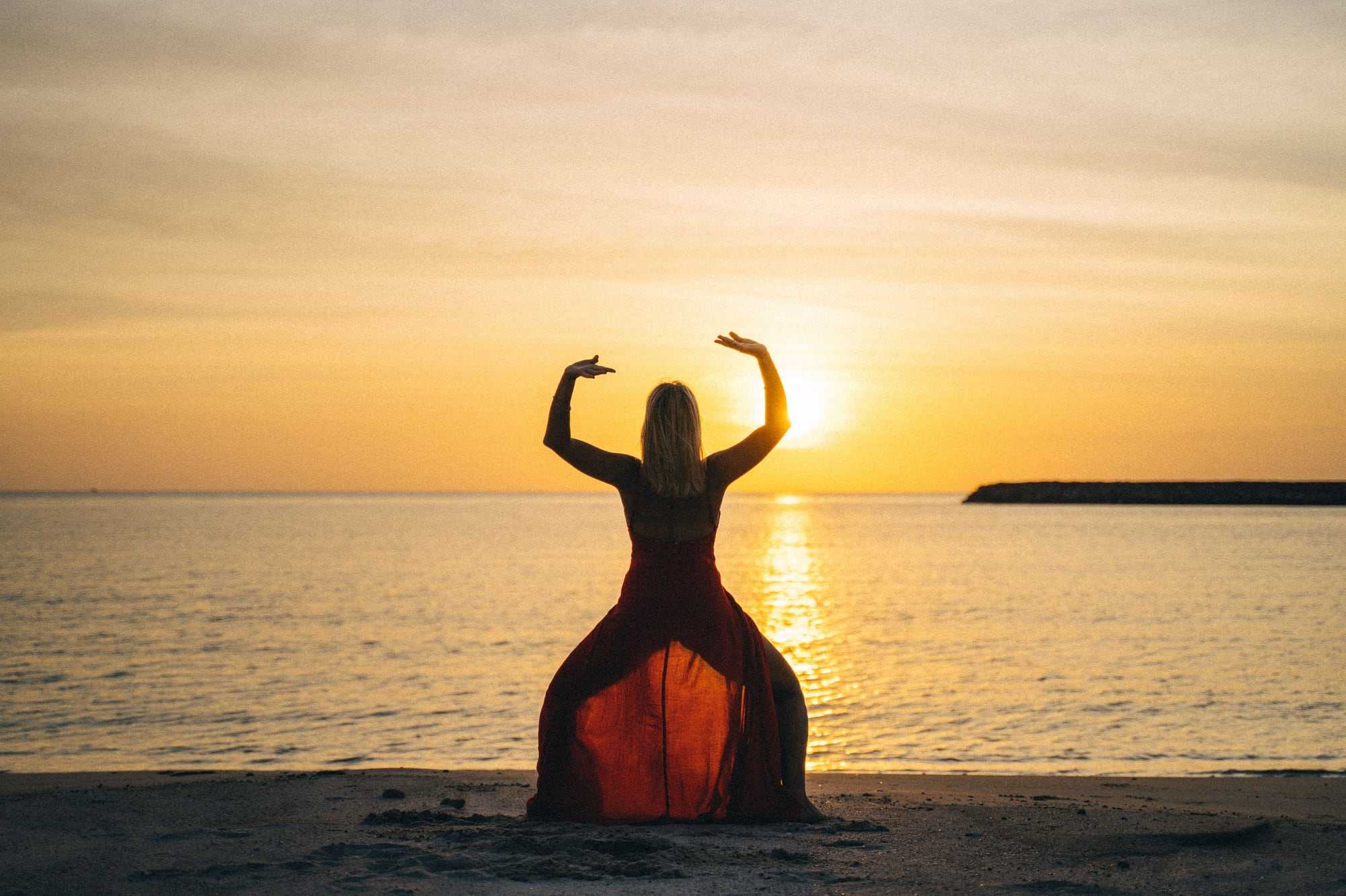 A person doing yoga on the beach at sunset, seen from behind